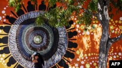 ILUSTRASI - Seorang perempuan melindungi wajahnya dari sinar matahari saat dia berjalan melewati dinding yang dihiasi mural Penduduk Asli Australia di ibu kota Darwin, 29 Agustus 2023.(DAVID GREY / AFP)