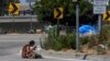 A homeless woman sits on the street at the entrance to an off-ramp to the CA-105 freeway next to a homeless encampment, July 26, 2024, in Los Angeles, California. 