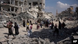 Palestinians walk through the destruction in the wake of an Israeli air and ground offensive in Khan Younis, southern Gaza Strip, April 8, 2024. Israel says it has withdrawn its last ground troops from the city, ending a four-month operation.