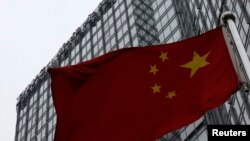 FILE - A building housing the PricewaterhouseCoopers (PWC) branch office stands behind a Chinese national flag in Beijing, Jan. 24, 2014. 