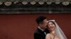 FILE - A bride and groom share a light moment with a sugar-coated Chinese haw as they pose during a pre-wedding photo shoot outside the Drum Tower in Beijing, April 23, 2023.