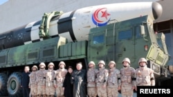 Pemimpin Korea Utara Kim Jong Un dan putrinya berfoto bersama sejumlah ilmuwan, pejabat militer dan insinyur yang terlibat dalam proyek uji coba rudal balistik antarbenua Hwasong-17 dalam foto yang yang dirilis pada 27 November 2022. (Foto: KCNA via Reuters)