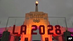 FILE - An LA 2028 sign is seen in front of the Olympic cauldron at the Los Angeles Memorial Coliseum, Sept. 13, 2017. 