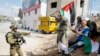 Demonstran memegang bendera Palestina di depan seorang tentara Israel yang memegang senjata saat protes menuntut Israel pembukaan kembali jalan yang ditutup menuju Nablus, di Deir Sharaf, di Tepi Barat yang diduduki Israel, 20 Oktober 2022. (Foto: Reuters)