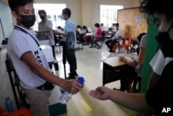 Seorang petugas pemilu menyemprotkan alkohol ke seorang pria sebelum dia memasuki kantor polisi untuk memilih di tempat pemungutan suara di distrik Tondo di Manila, Filipina pada Senin, 9 Mei 2022. (Foto: AP)
