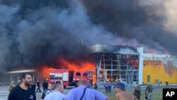 Sejumlah warga menyaksikan asap yang keluar dari pusat perbelanjaan di Kota Kremenchuk, Ukraina, yang diserang oleh rudal milik pasukan Rusia pada 27 Juni 2022. (Foto: Viacheslav Priadko via AP)