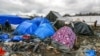 Migrants walk among tents in a muddy field at a camp of makeshift shelters for migrants and asylum-seekers from Iraq, Kurdistan, Iran and Syria, called the Grande Synthe jungle, near Calais, France, Feb. 3, 2016. 