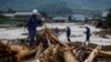 Pihak kepolisian Jepang berjalan di atas puing-puing kayu yang tersapu hujan lebat saat mereka melakukan operasi penyelamatan dan pencarian di Asakura, Prefektur Fukuoka, Jepang, 8 Juli 2017.