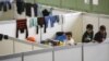 FILE - Children watch as they stand on beds in a shelter for migrants inside a hangar of the former Tempelhof airport in Berlin, Germany, Dec. 9, 2015. 