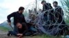 Syrian refugees cross into Hungary underneath the border fence on the Hungarian-Serbian border near Roszke, Hungary, Aug. 26, 2015. 