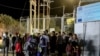 Refugees and migrants stand at the closed gate of the Moria migrant camp, after a fire at the facility, on the island of Lesbos, Greece, Sept. 19, 2016. 