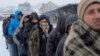 Migrants wait in line to receive plates of free food during a snowfall outside a derelict customs warehouse in Belgrade, Serbia, Jan. 18, 2017. 