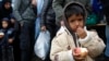 A child eats an apple waiting in line to cross the Serbian-Croatian border, at the village of Berkasovo, near Sid, Serbia, Oct.15, 2015.