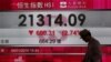 A man walks past a panel displaying the benchmark Hang Seng index during afternoon trading in Hong Kong, China, Jan. 4, 2016. 