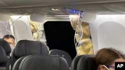 This image provided by Kelly Bartlett shows passengers near a hole in the fuselage of an Alaska Airlines Boeing 737 Max 9, Flight 1282, which was forced to return to Portland International Airport, Jan. 5, 2024. 