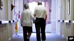 FILE - Decima Assise, who has Alzheimer's disease, and Harry Lomping walk the halls at The Easton Home in Easton, Pennsylvania, Nov. 6, 2015.