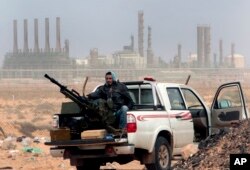 FILE - An anti-government rebel sits with an anti-aircraft weapon in front of an oil refinery in Ras Lanouf, eastern Libya, March 5, 2011.