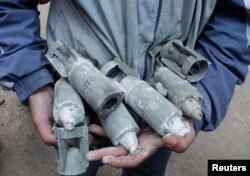 FILE - A boy holds unexploded cluster bombs after jet shelling by forces loyal to Syria's President Bashar al-Assad in the al-Meyasar district of Aleppo February 21, 2013.