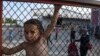 FILE - A child stands behind a fence at the Oreokastro camp, near the northern town of Thessaloniki, Greece, June 25, 2016.
