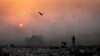 FILE- A thick blanket of smoke is seen against the setting sun as young ragpickers search for reusable material at a garbage dump in New Delhi, India, Oct. 17, 2014.