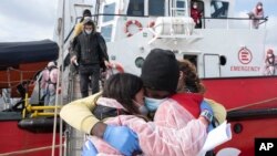 Seorang migran memeluk anggota LSM saat turun dari kapal penyelamat Open Arms, di Pelabuhan Augusta, Sisilia, setelah diselamatkan di laut, Sabtu, 12 Maret 2022. (Foto: AP)